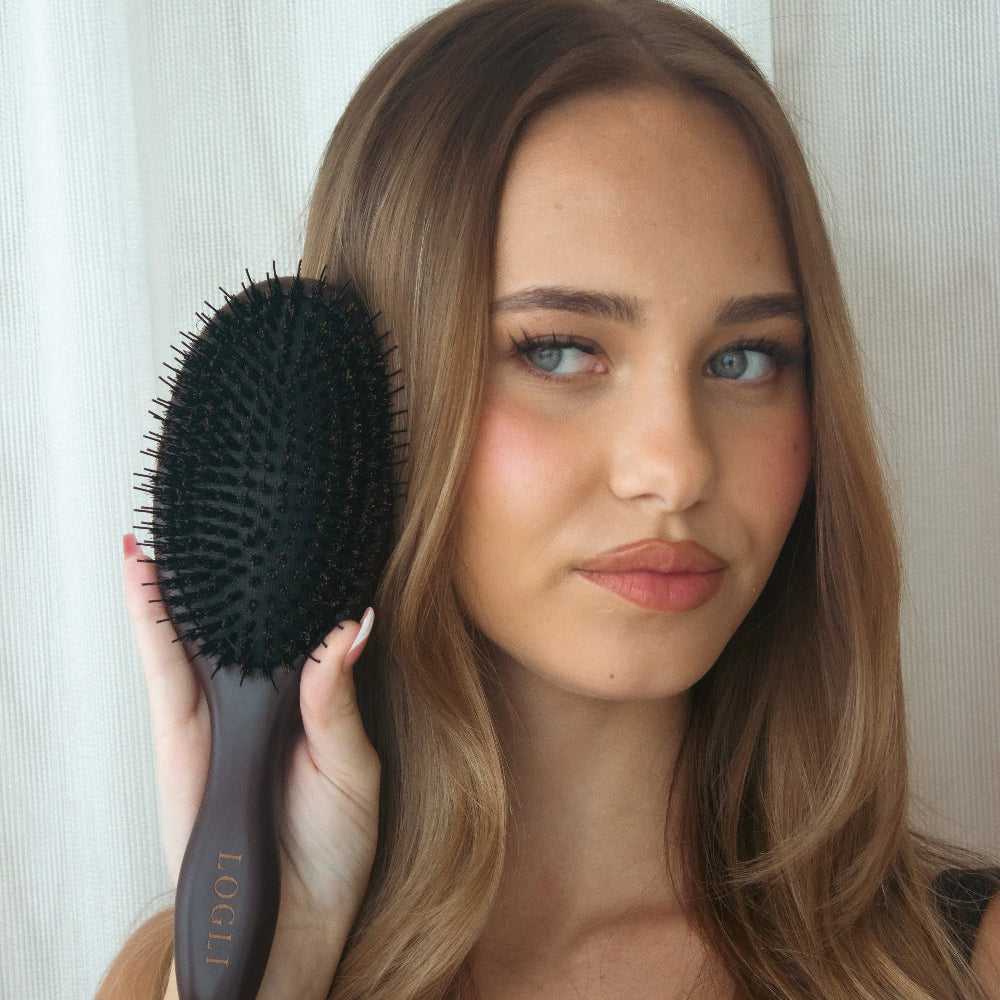 Woman holding a burgundy hairbrush with a white curtain background