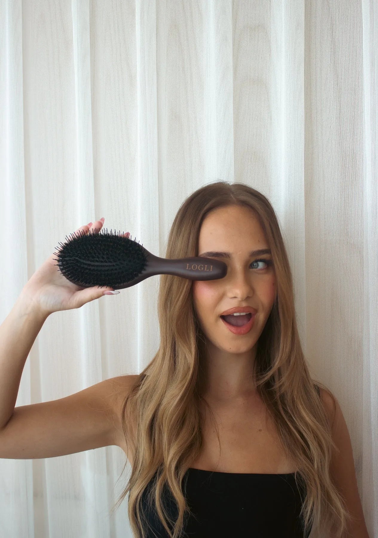 Woman holding a hairbrush in front of a white curtain