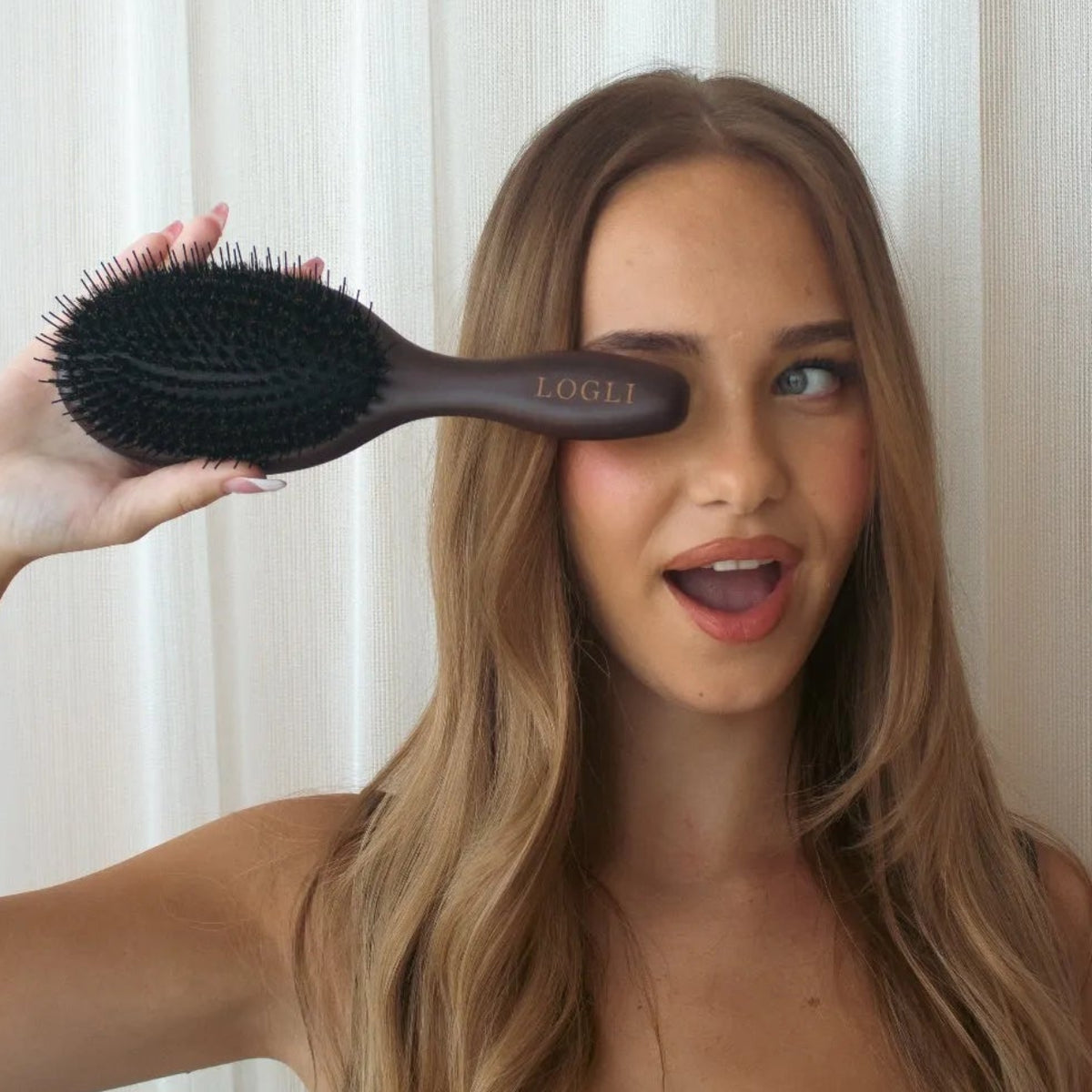 Woman holding a hairbrush in front of a white curtain