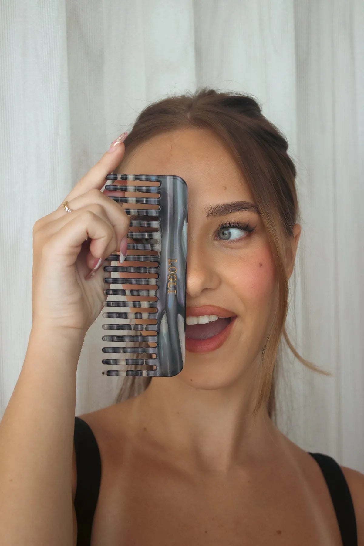 Woman holding a zebra comb in front of her face with a white curtain background