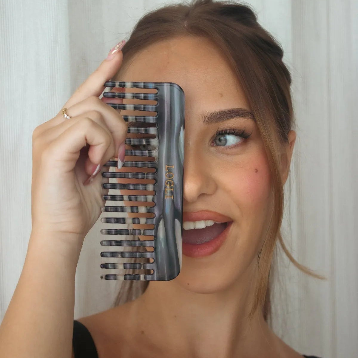 Woman holding a zebra comb in front of her face with a white curtain background
