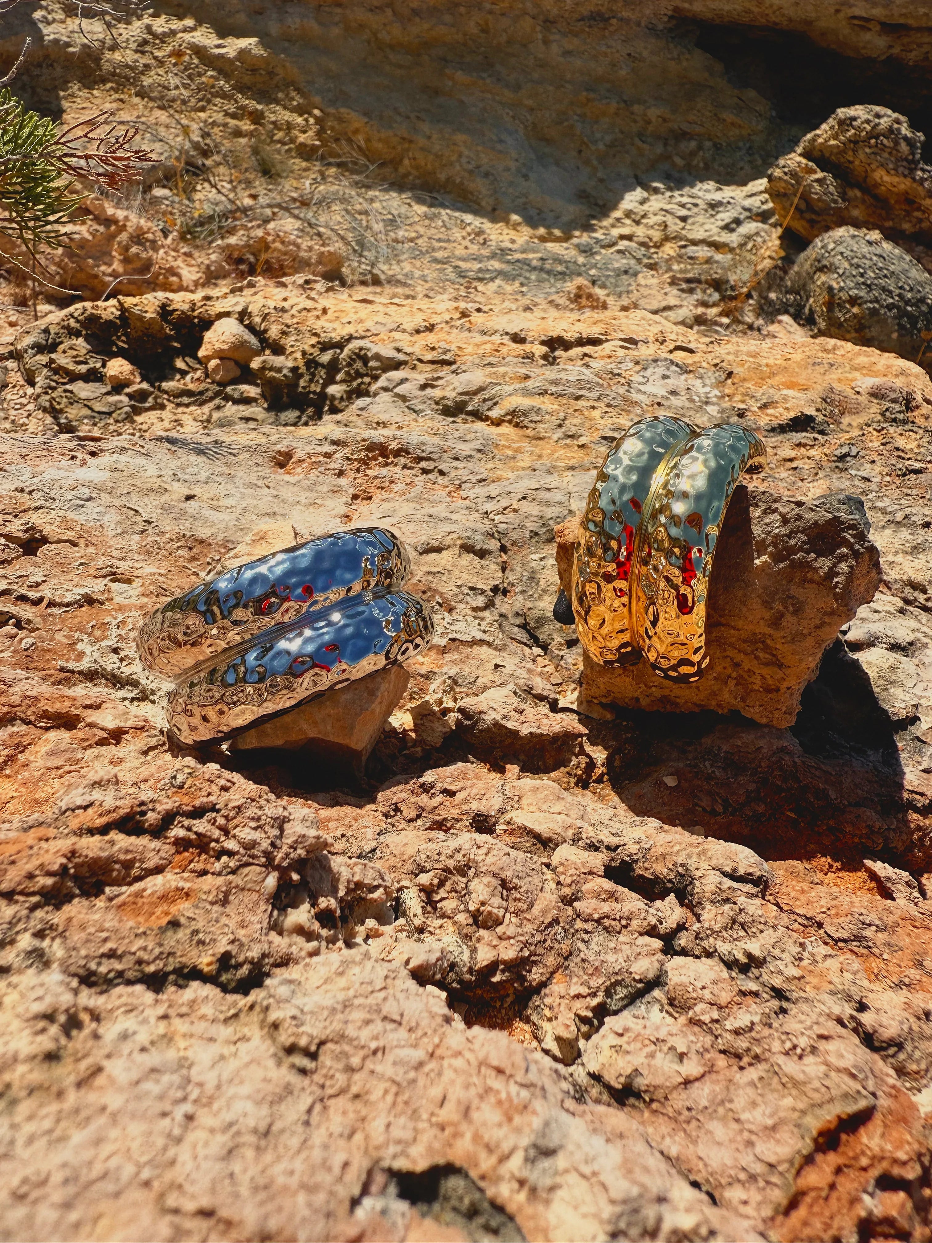 Two metal cuffs with silver and gold accents on a rocky surface