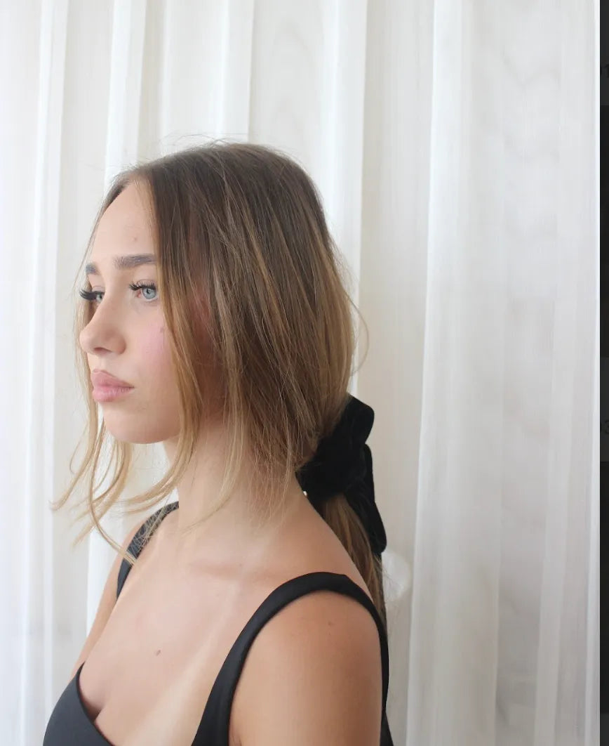 Woman with a black bow in her hair against a white curtain background