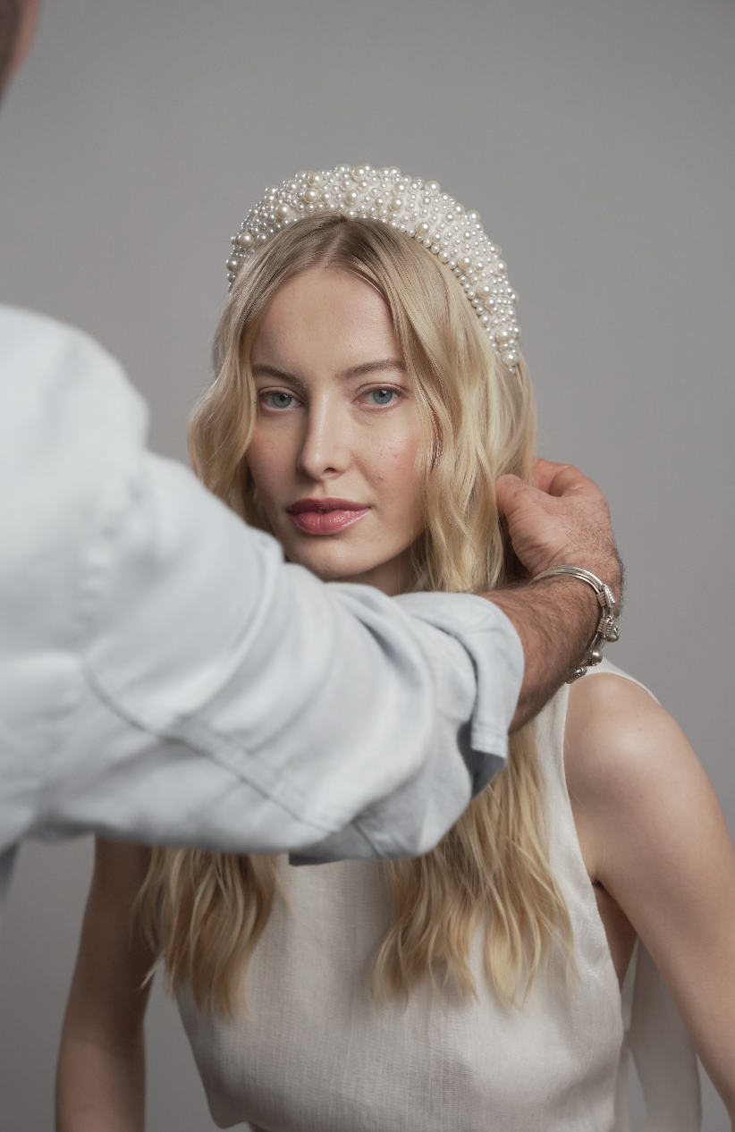 Person adjusting a sparkling headband on another person against a neutral background