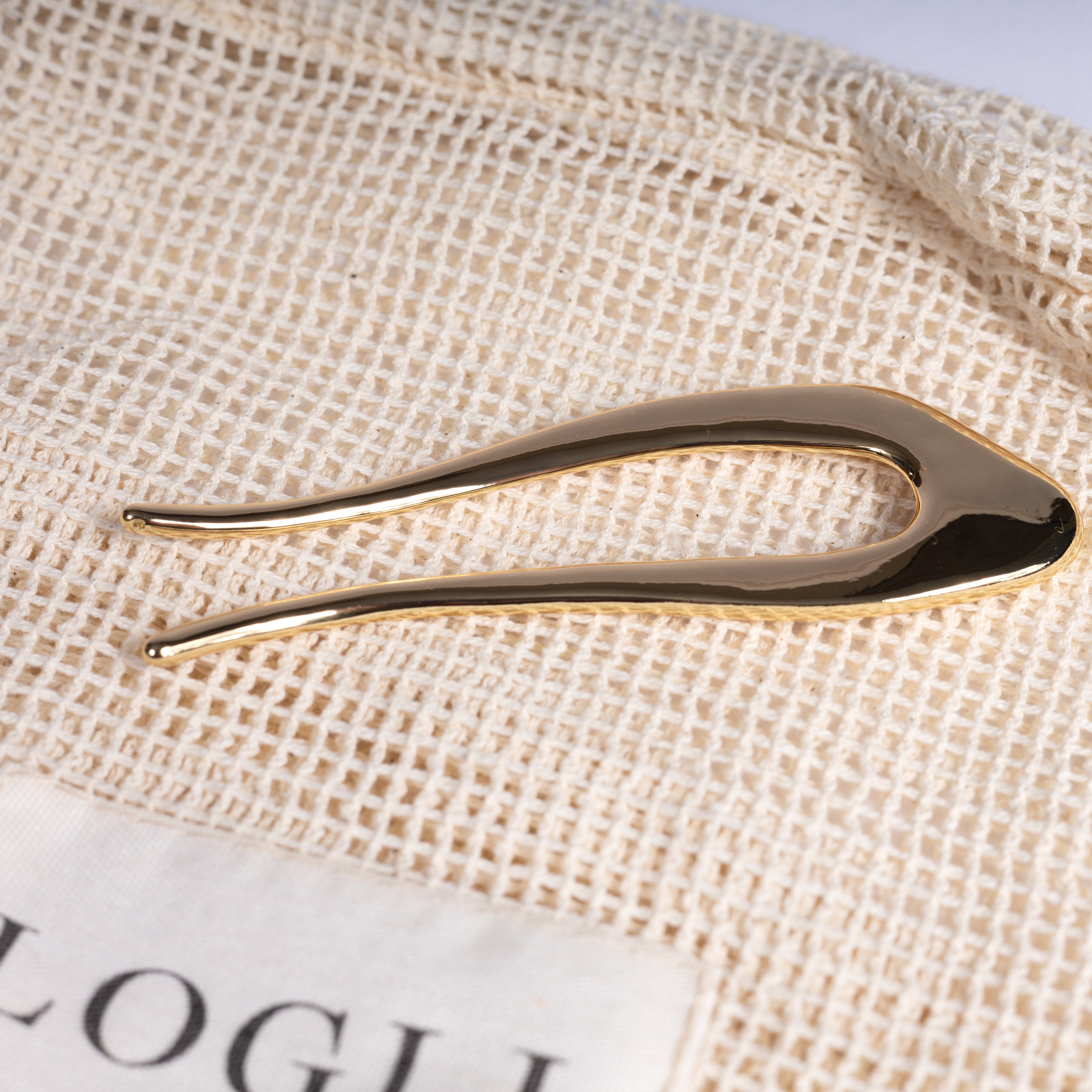 Gold hair clip on a textured beige fabric with a visible brand label.