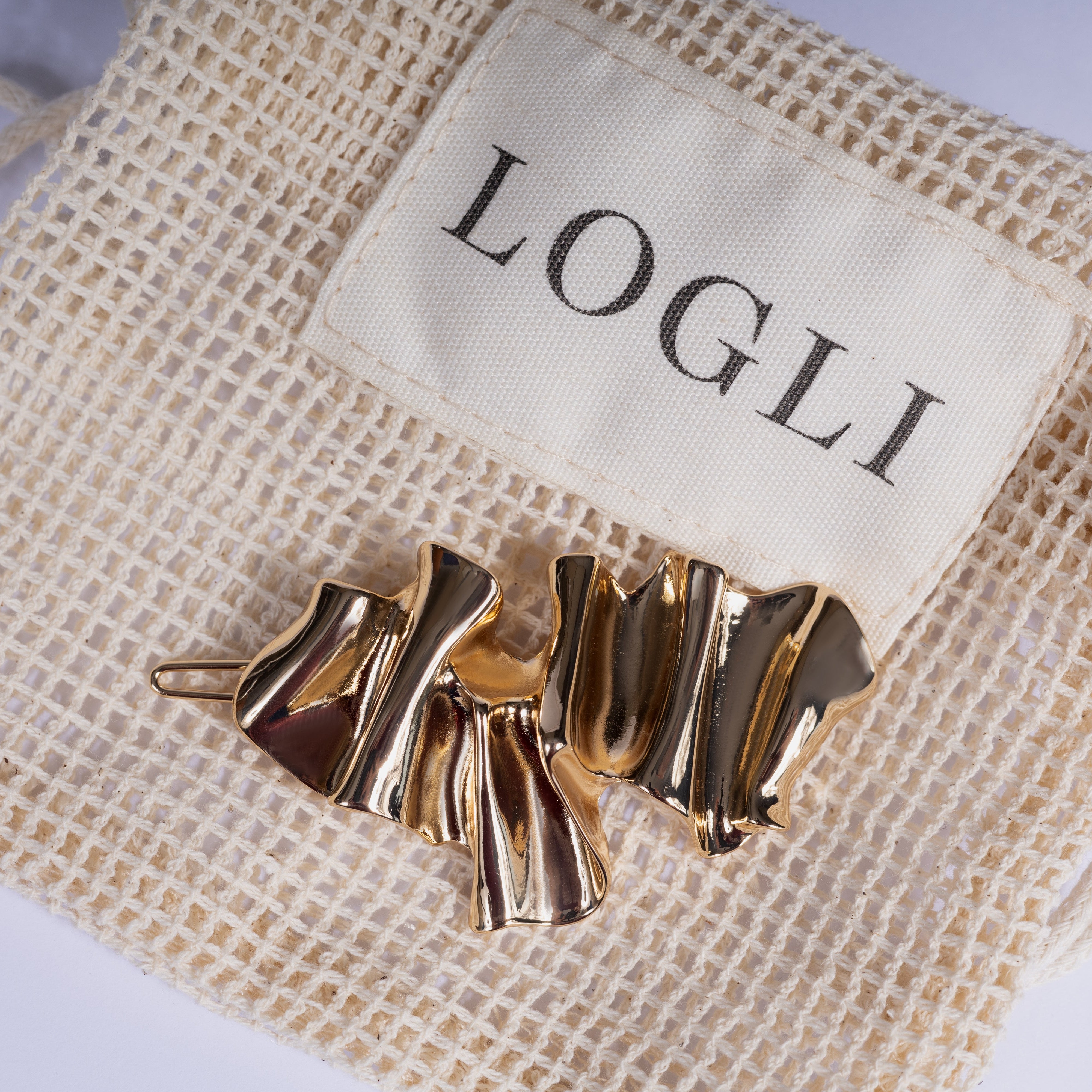 Gold hair clip on a beige drawstring bag with 'LOGLI' branding.
