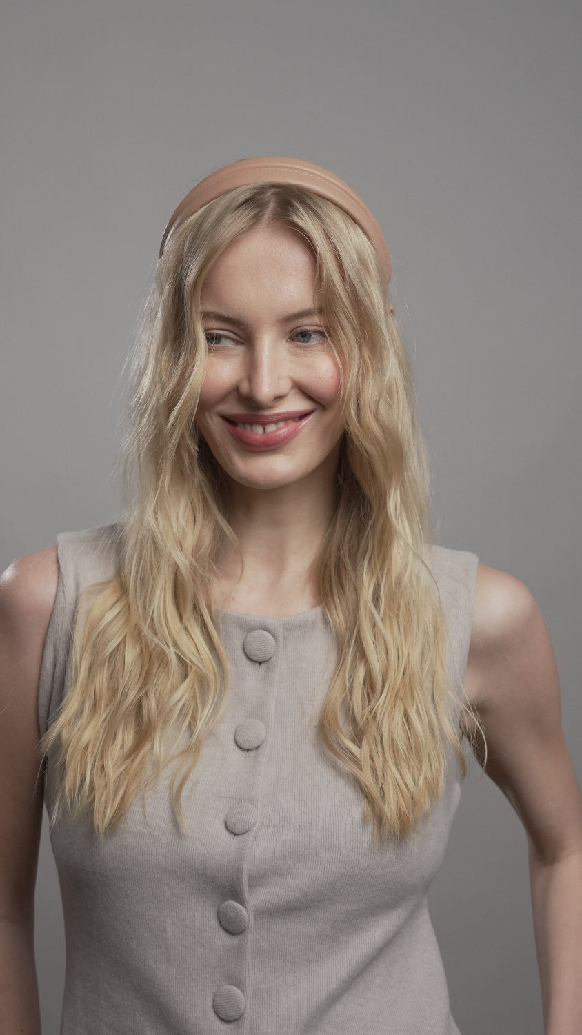 Woman with blonde hair wearing a beige coat against a gray background