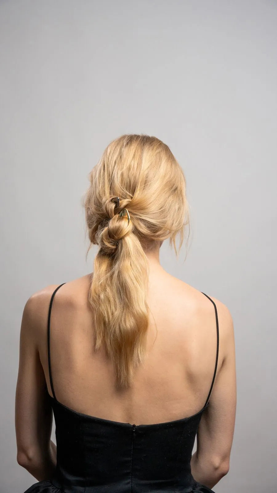 Woman with a stylish hair bun wearing a black dress against a gray background