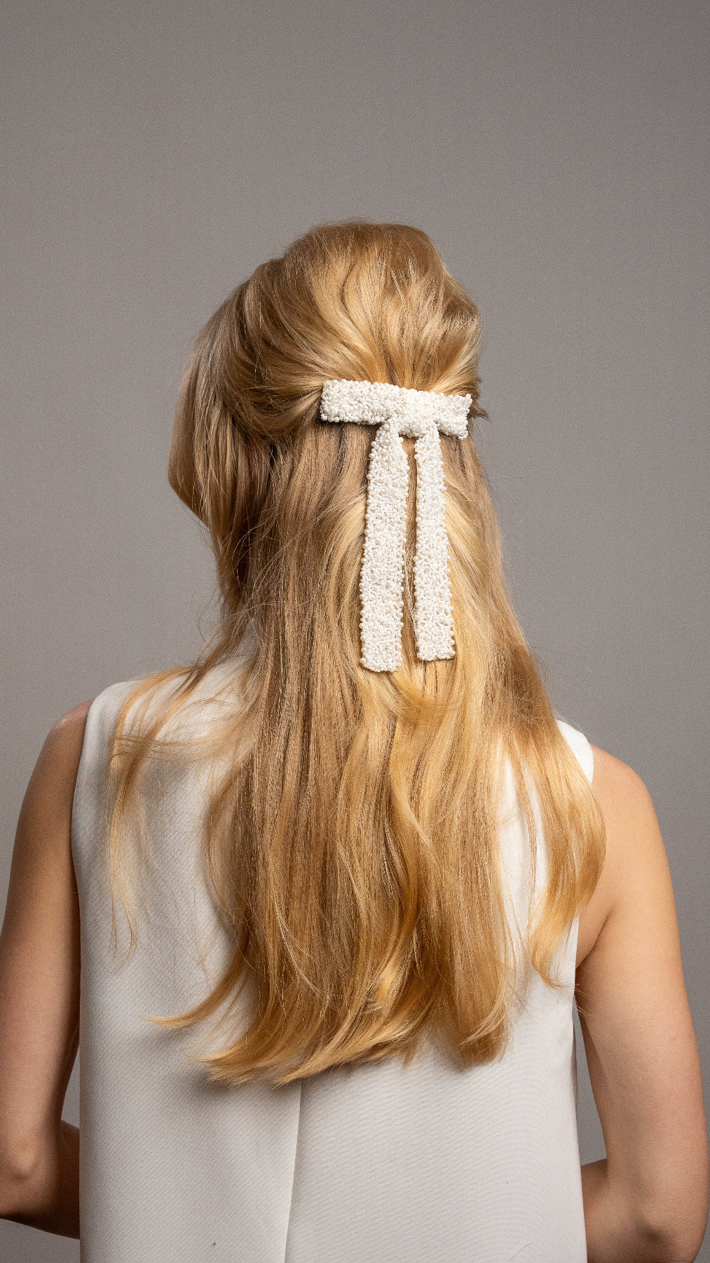 Woman with long blonde hair wearing a decorative hair clip against a gray background