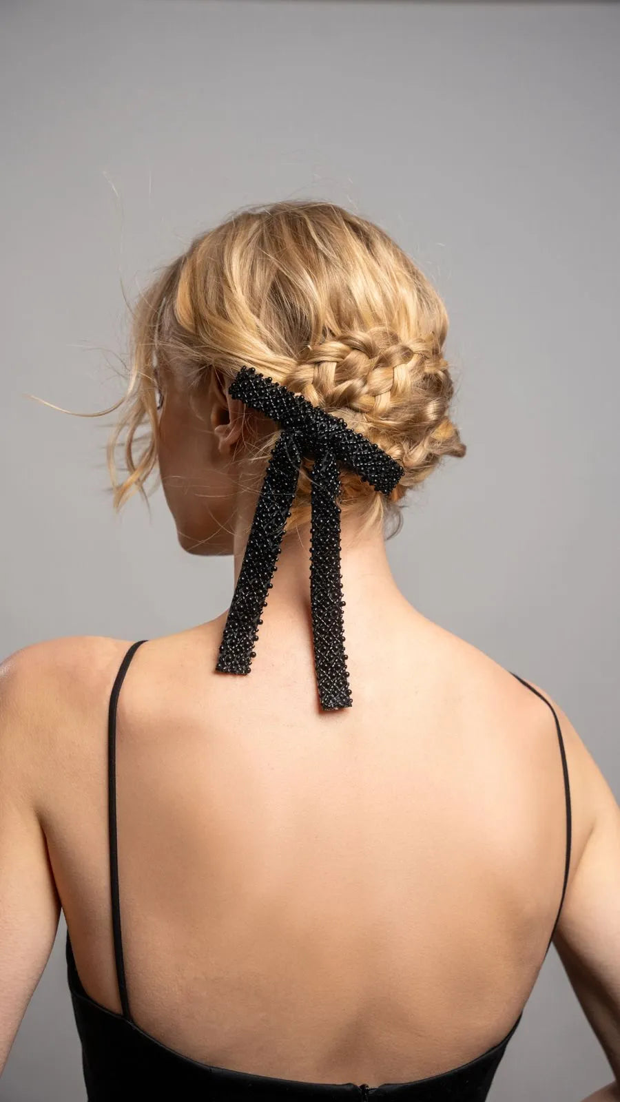 Woman with braided hair wearing a black hair accessory against a gray background