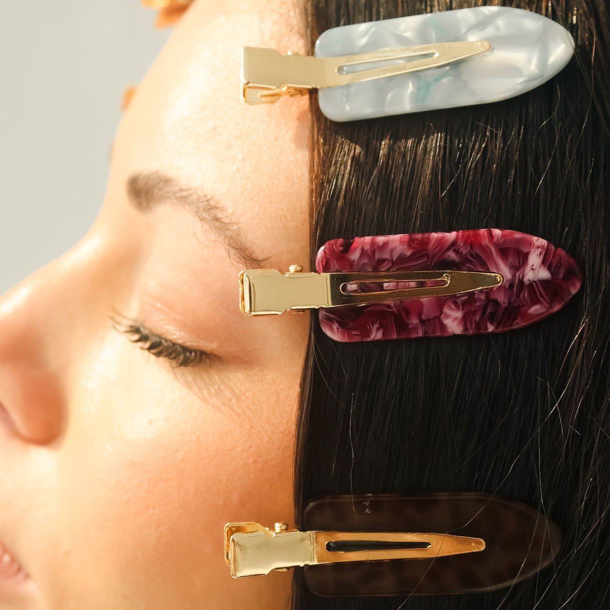 Three tortoiseshell hair clips with gold-tone metal clasps shown attached to a person's dark hair against a light gray background.