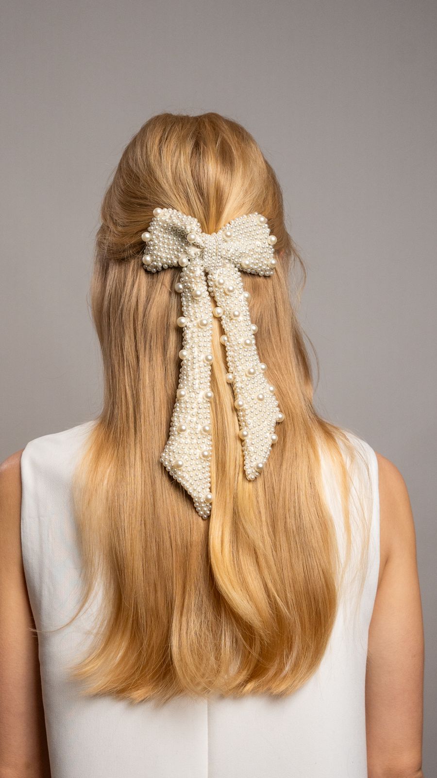 Woman with long blonde hair wearing a decorative pearl hair bow against a gray background
