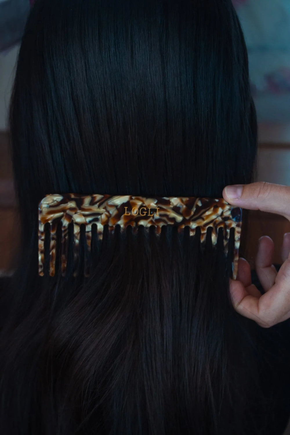 Person holding a leopard print comb with 'LOGLI' branding in dark hair.