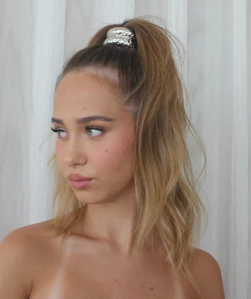 Woman with metal cuff in a high ponytail against a white curtain background