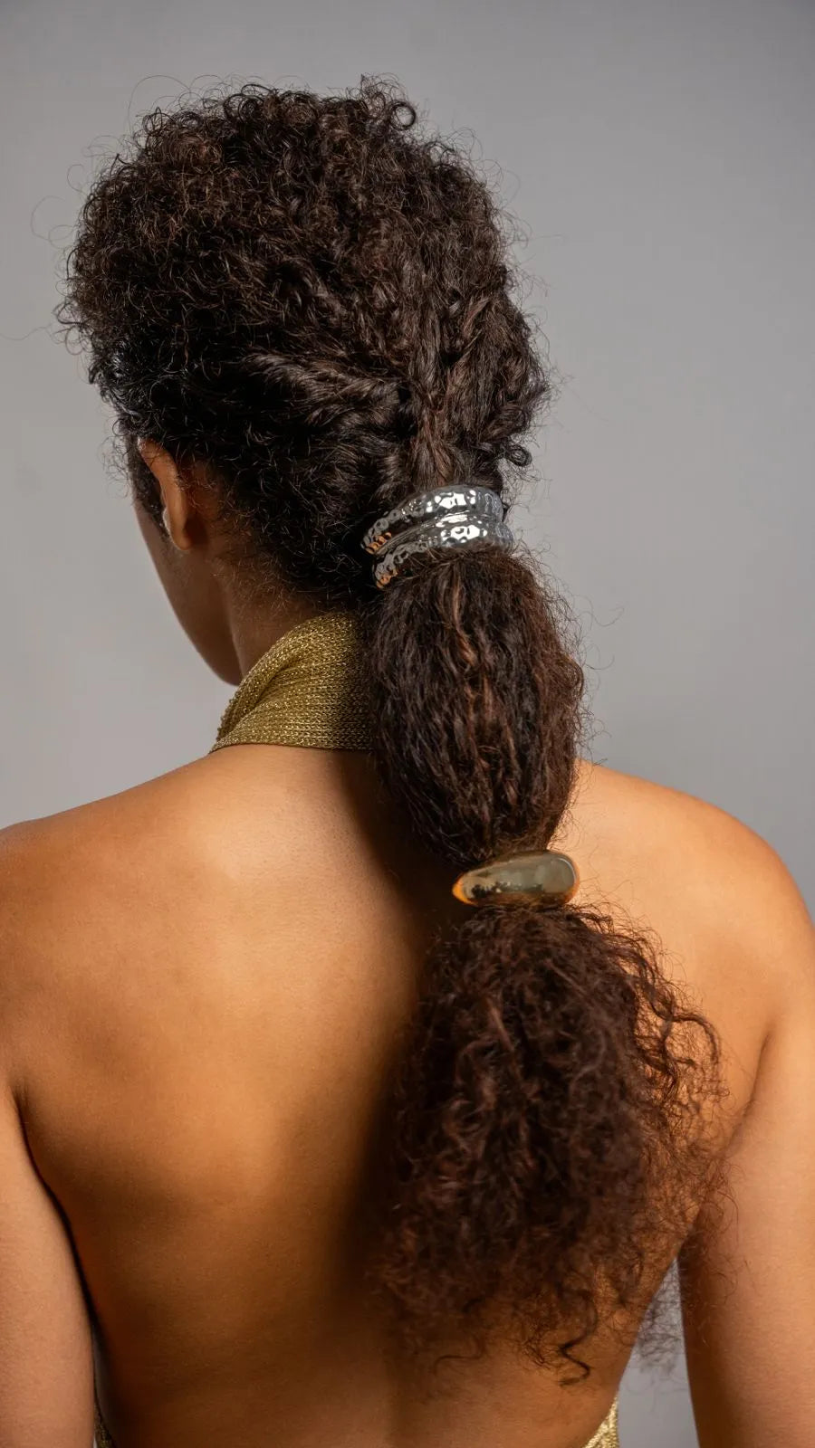 Person with styled hair in a high ponytail wearing a green headband against a gray background