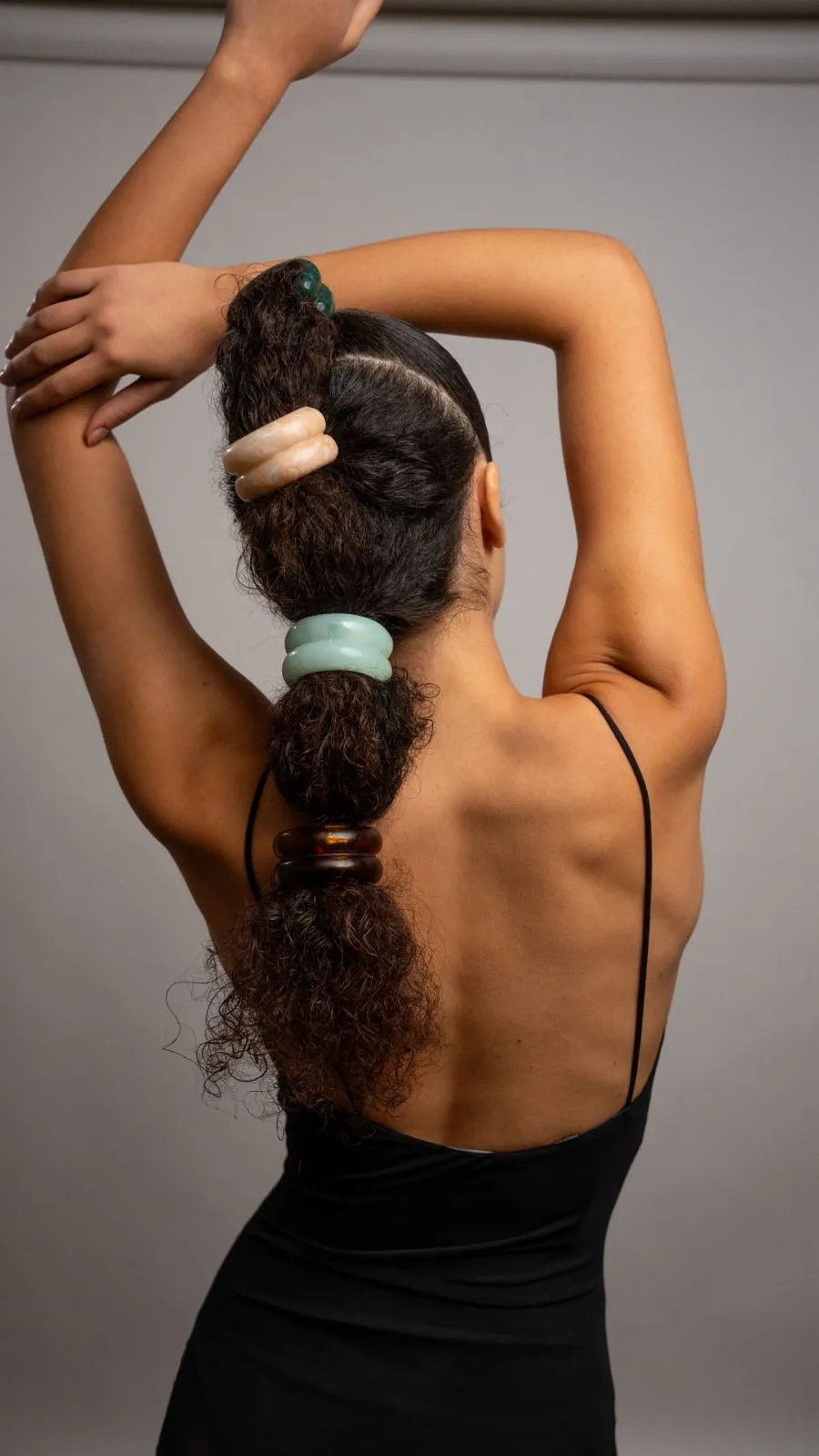 Woman with styled hair wearing a black dress against a gray background