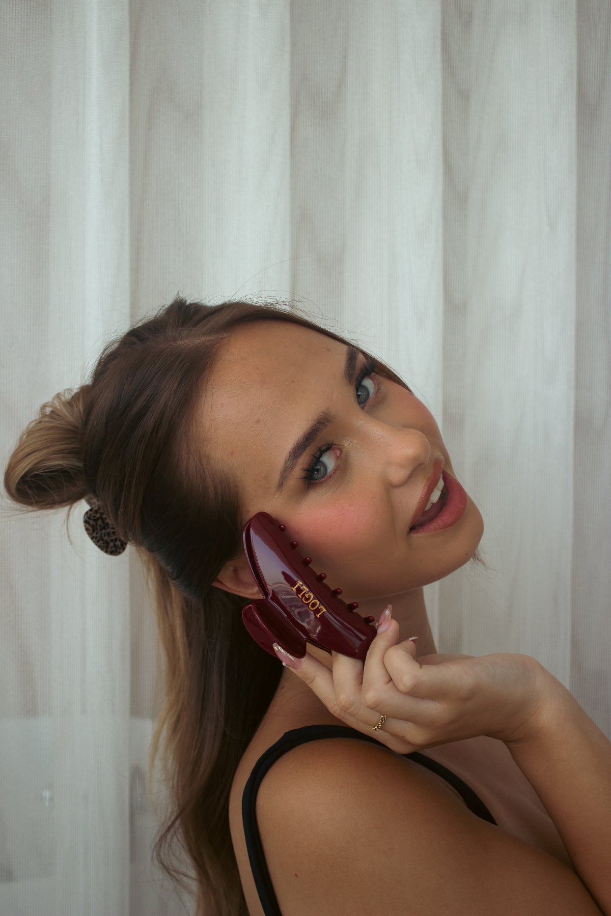 Woman holding a burgundy claw against a white curtain background